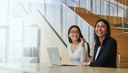 Two smiling business women meeting and working on a laptop
