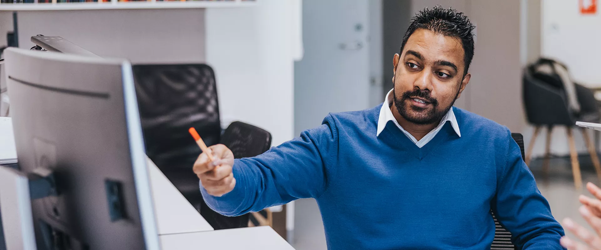 A man, seated in an office, pointing at a computer screen
