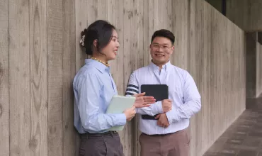 Two business people smiling and standing against a wall