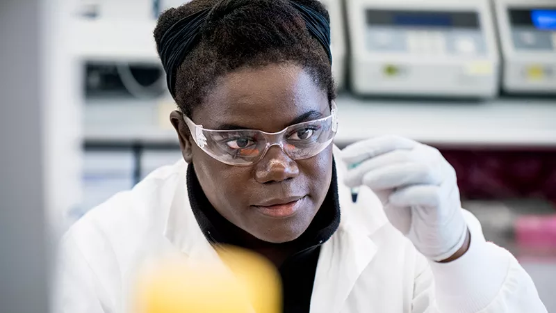 Novartis researcher is working on developing a new medicine. A researcher at Novartis wearing safety glasses is looking at test tube.