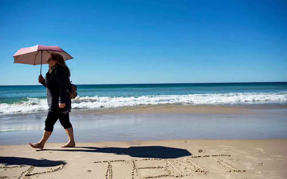 Woman walks along the beach holding an umbrella. Woman walks along the beach holding an umbrella to protect herself from the sun.