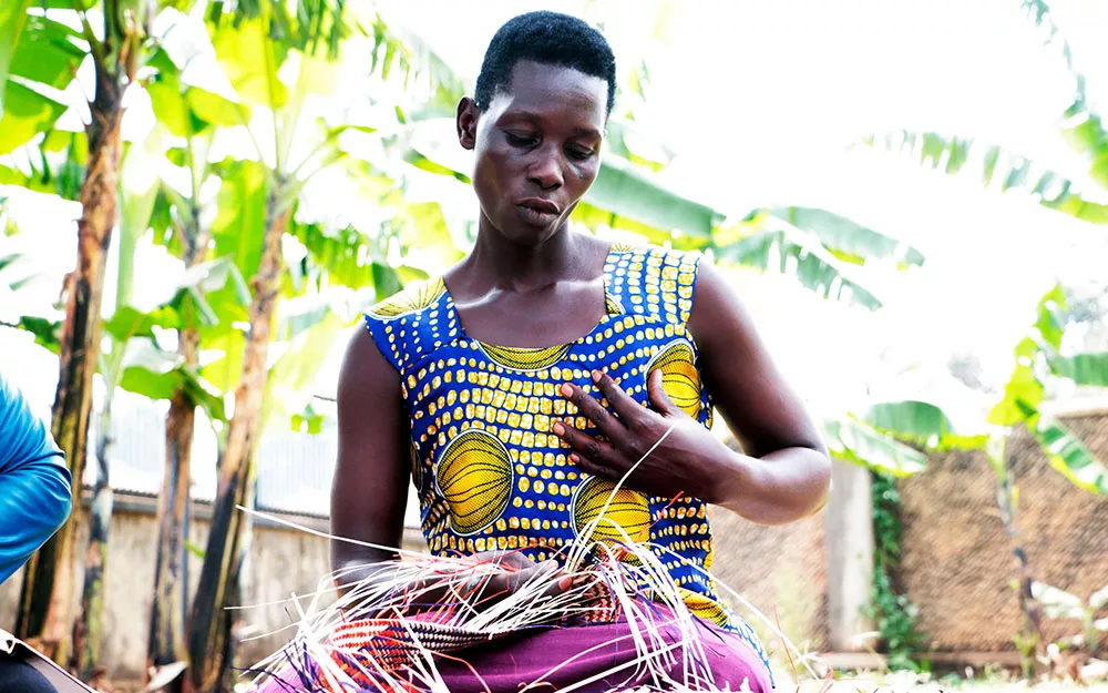 Akello sits in a garden waving a mat Akello sits in a garden waving a mat