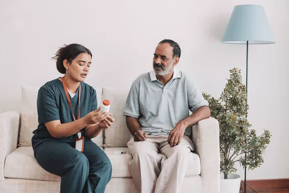 A female health worker talking a male patient through his medication steps and holding a bottle of pills in her hand. A female health worker talking a male patient through his medication steps and holding a bottle of pills in her hand.
