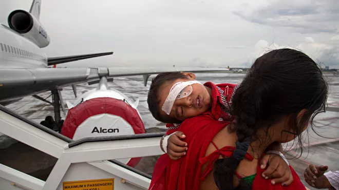 Woman carrying child with eye bandage off airplane