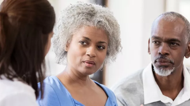 A woman, accompanied by her caregiver, shares her experiences with a doctor.