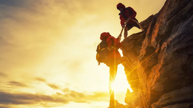 Two climbers working together to climb up a rock face.