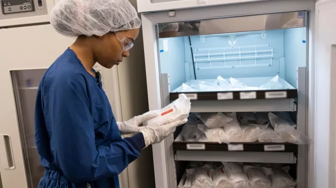 An associate in personal protective equipment stands at a refrigerator examining a bag